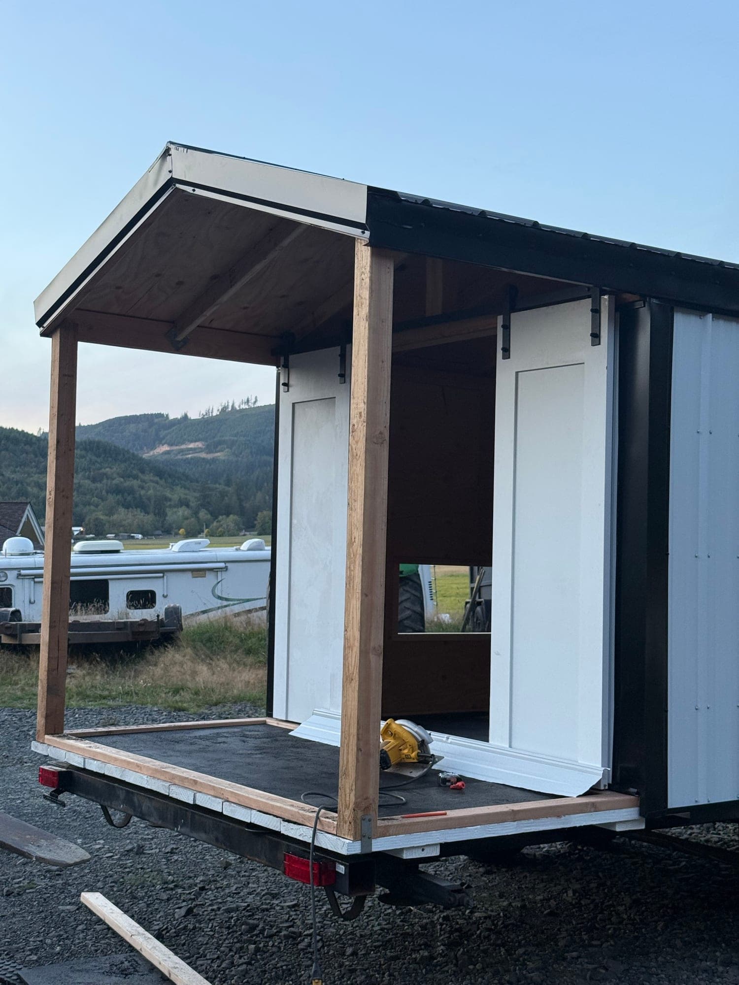 The porch roof trimmed out and the deck being finished outdoors, with hills behind